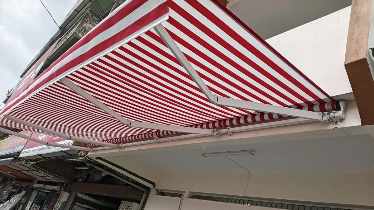 The underside of a red and white striped awning, showing its folding arms and the roller on the wall