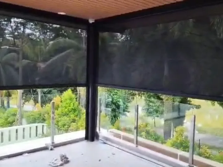 Looking out from a balcony through a dark zip blind, with palms and a lake still visible beyond
