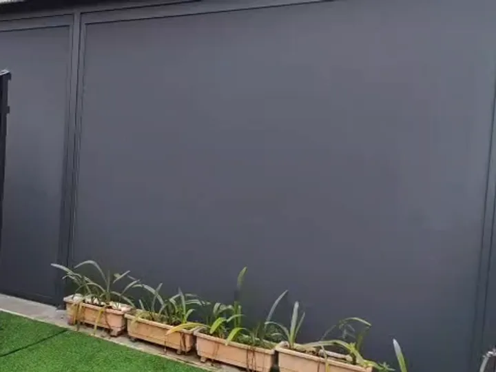 A dark grey zip blind closing the side of a car porch beside a lawn and potted plants