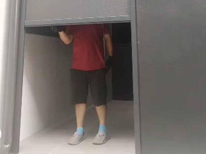 The bottom bar of a tall dark grey zip blind being raised in a narrow side opening, with a person standing under it