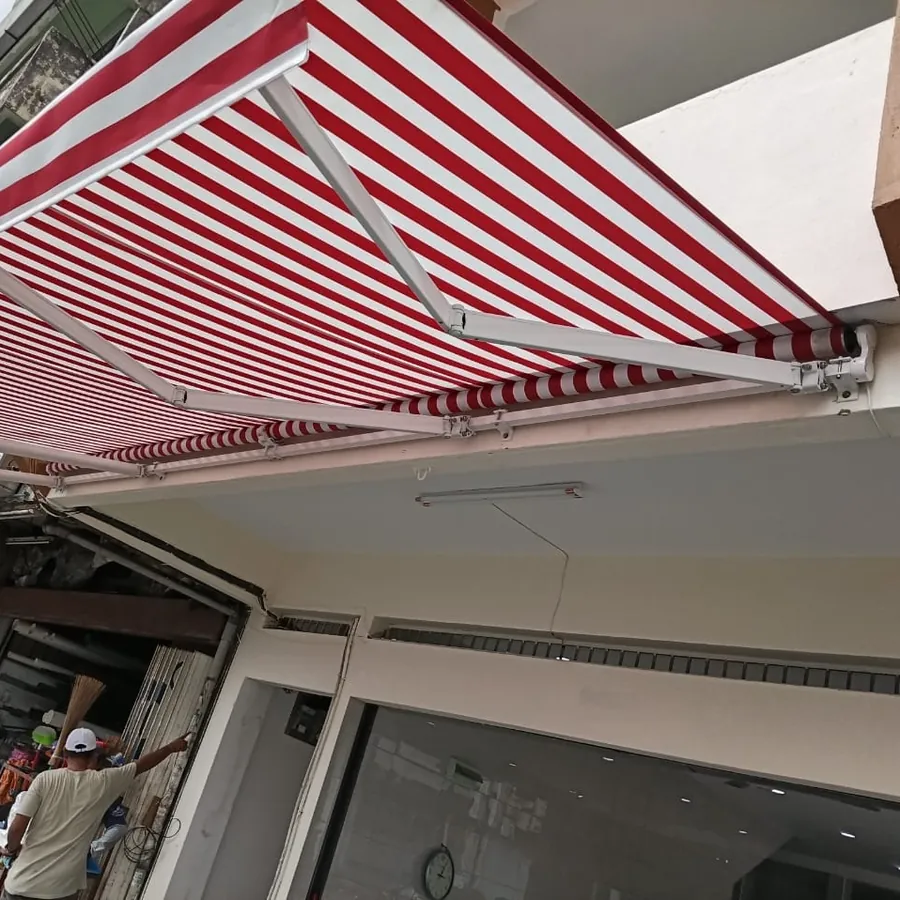 The underside of a red and white striped awning, with its arms and roller